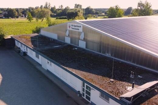 Dachansicht eines Sportgebäudes mit Solarpanelen und begrüntem Dach, umgeben von Wiesen und Bäumen.