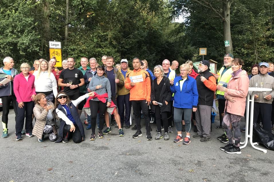 Gruppe von Laufenden und Zuschauern versammelt in einem Waldgebiet, zeitweise von einem Verkehrsschild umgeben.